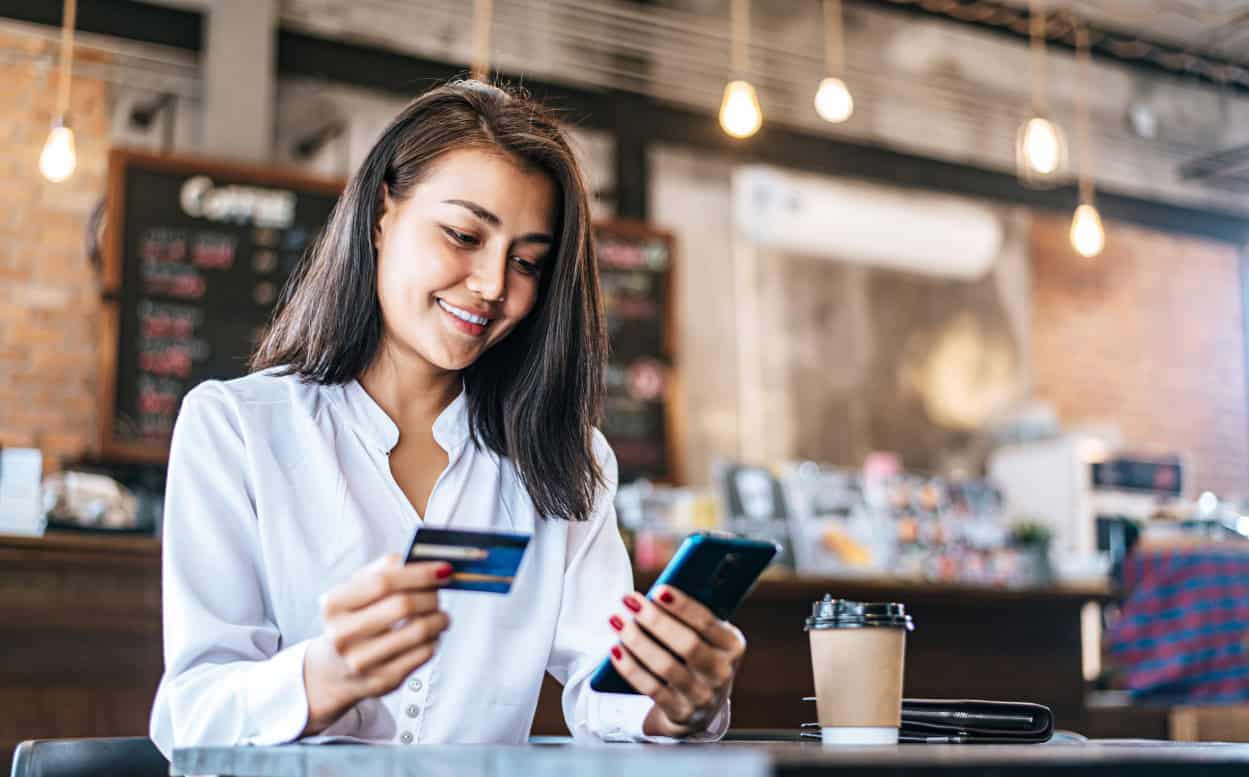 a lady holding her phone in one hand and her credit card in the other while paying for her coffee